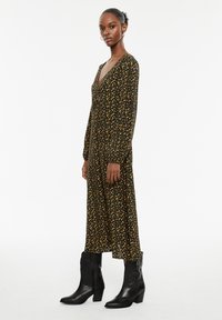 Zwarte bloemenjurk met lange mouwen en een diepe v-hals, versierd met gele bloemen. Gecombineerd met zwarte cowboylaarzen.