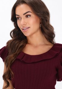 Top ribbed burgundy, cu un guler rotund larg și accente de umăr volanate, având o textură moale și o siluetă ajustată.