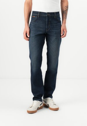 Jeans de mezclilla azul oscuro con corte recto, que presentan un diseño clásico de cinco bolsillos y un sutil parche con el logotipo en la pretina.