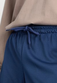 Shorts de sport en maille bleu marine avec une taille élastique, dotés d'un cordon de serrage pour un ajustement réglable, accompagnés d'un haut marron clair.