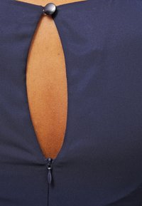 Navy blue top featuring a keyhole cutout detail secured with a round black button, complemented by a short zipper at the bottom.