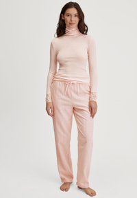 Roze geribbelde coltrui en geruite pyjamabroek met kantaccenten op de mouwen. Zachte stof, losse pasvorm en koordje in de taille.