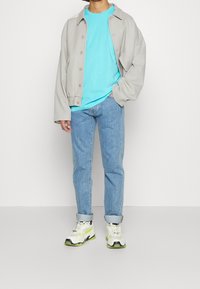 Světlě šedá oversized bunda, aqua modré tričko, světle modré džíny a bílé tenisky s černými a neonově zelenými akcenty. Strukturovaný design.