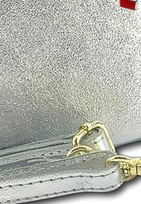 Metalen zilveren leren tas met een gladde textuur, gouden hardware-details en een contrasterende rode accent. Ritssluiting met een afneembare schouderband.