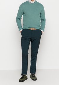 Suéter de punto verde claro con cuello redondo, combinado con pantalones azul verdoso oscuros y zapatillas verdes. Patrón texturizado notable en el suéter.