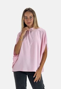 Top rosa, ligero, con cuello alto y ajuste holgado. Cuenta con mangas remangadas y un acabado texturizado. Combinado con jeans oscuros.