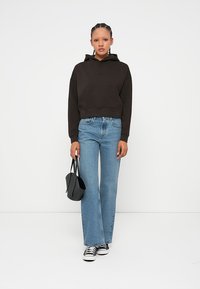 Hoodie cropped preto com um bolso frontal, combinado com jeans flare de tom azul claro. O look é complementado por ténis pretos e uma pequena mala preta.