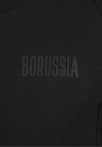 Tessuto nero con lettere nere in rilievo che scrivono "BORUSSIA" centrato sulla superficie.