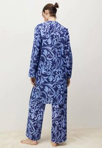 Lange mouwen blauwe pyjama set met een bloemenpatroon in tinten lichtblauw. Losvallende top en broek met wijde pijpen van zachte stof.