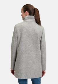 Cappotto di lana grigio con colletto alto, vestibilità ampia e design a lunghezza media, caratterizzato da una trama sottile e senza chiusure visibili.