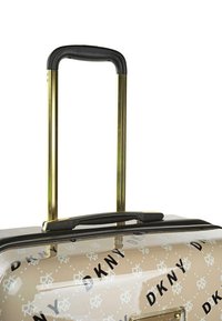 Maleta rígida en color beige con patrón de logo de DKNY. Cuenta con un mango telescópico dorado con empuñadura negra y cierre de cremallera.