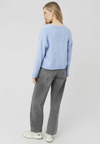 Pull en tricot bleu clair avec une coupe décontractée, un ourlet côtelé et des épaules tombantes, associé à un jean en denim gris taille haute et des baskets blanches.