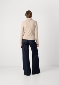 Beige Langarmoberteil mit gerippter Textur und Kragen, kombiniert mit dunkelblauen weitem Jeans, die Rückentaschen und Kontrastnähte aufweisen.