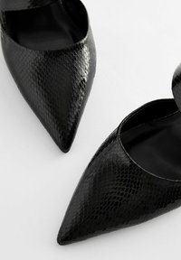 Svarta spetsiga skor med en blank, texturerad ormskinnsmönster. Har en slip-on-design med öppna sidor och en slät inredning.