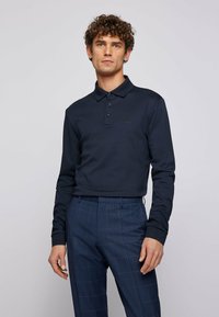 Navy long-sleeve polo shirt with a collar, three buttons, and a subtle logo. Paired with checked trousers in darker blue tones.
