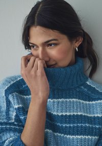 Strickpullover mit hohem Kragen, ausgestattet mit blauen und hellblauen horizontalen Streifen; weiche Textur, gerippte Details, körpernahe Passform.