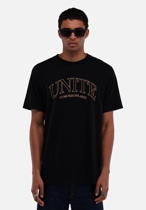 Zwarte katoenen t-shirt met bold "UNITE" en "TOMORROWLAND" tekst in gouden borduursel, korte mouwen, ronde hals en een relaxed fit.