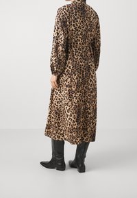Ruskean ja mustan värin leopardikuvioinen pitkähiha dress, jossa on vyötäröä korostava malli, valuva siluetti ja elastiset hihansuut, yhdistettynä mustiin polvimittaisiin saappaisiin.