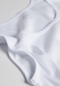 Hvid stof tanktop med en glat tekstur, der har subtil ribbning og en buet halsudskæring. Inkluderer et lille logo-detalje.