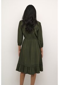 Olive green dress with three-quarter sleeves, elastic waist, and ruffled hem. Features lace-like accents along the shoulders and skirt.