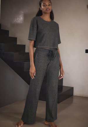 Grau gestreiftes Strick-Loungewear-Set bestehend aus einem verkürzten Oberteil mit kurzen Ärmeln und einer Hose mit Kordelzug, beide aus einem weichen Material und mit lockerer Passform.