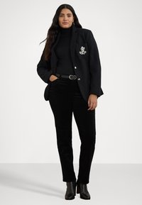 Svart blazer med en lapp lomme, båret over en svart turtleneck. Kombinert med svarte cordbukser og hælankelstøvler, noe som skaper et monokromt utseende.