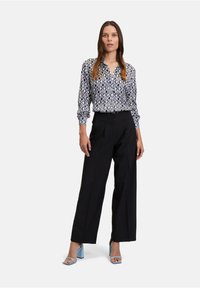 Koszula z guzikami w niebiesko-białym geometrycznym wzorze, w połączeniu z czarnymi spodniami o szerokich nogawkach i jasnoniebieskimi sandałami na słupku.