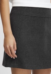 Grå ullkjol med en slät textur, som har en enkel design, subtila sömmar och en rak nederkant. Lommmen syns.