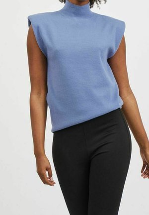 Jasnoniebieski bezrękawnik z wysokim, sztucznym kołnierzem i wyraźnym fasonem ramion, zestawiony z czarnymi dopasowanymi spodniami.