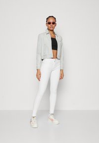 Svjetloplava skraćena jakna, crni crop top, bijele uske traperice i šarene tenisice s ružičastim akcentima. Naočale za sunce s ružičastim nijansama.