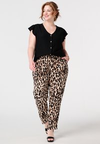 Haut à manches courtes noir à boutons avec un tissu texturé, associé à un pantalon beige à imprimé léopard doté de poches latérales et d'une coupe décontractée.