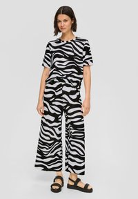 Ensemble bicolore en imprimé zèbre, comprenant un haut ample à manches courtes et un pantalon à jambes larges, associé à des sandales à plateforme noires.