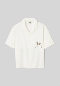 Chemise blanche à manches courtes, boutonnée, col avec un petit dessin linéaire marron représentant une plante et un vase sur la poche poitrine gauche.