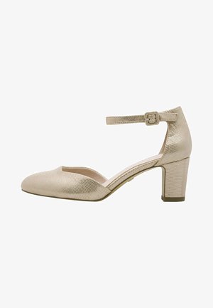 Beżowe lakierowane czółenko z teksturowanym wykończeniem, zamkniętym noskiem, wycięciami po bokach i niskim słupkowym obcasem. Pasek wokół kostki z kwadratową klamrą.