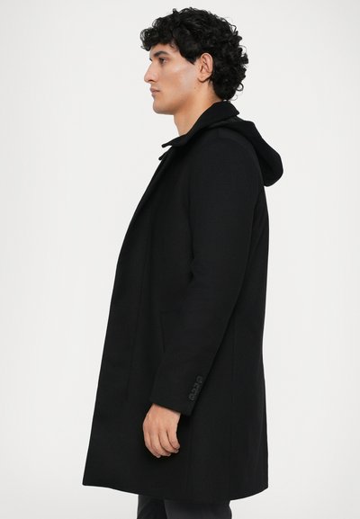 Abrigo negro con capucha, con un diseño entallado, bolsillos laterales y puños abotonados. La tela parece suave con una silueta estructurada.