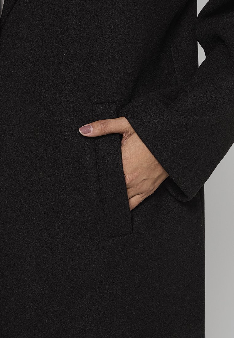 Zwarte wollen jas met een zachte textuur, voorzien van een zijzak en een recht gesneden ontwerp. De mouw is iets losjes, wat comfort biedt.