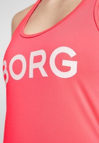 Růžový sportovní top vyrobený z hladké látky, s velkými bílými perforovanými písmeny, které na hrudi hlásí "BORG".