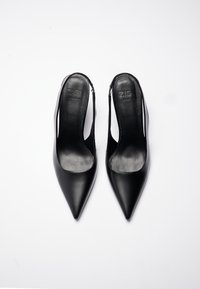 Black leather slingback heels with a pointed toe, smooth texture, open sides, and a minimalist design. Brand logo visible on the insole.