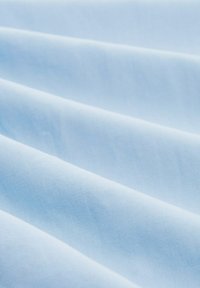 Tissu bleu clair avec une texture lisse, présentant des plis et des rides doux qui créent un effet de vagues subtil sur la surface.