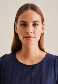 Blusa blu navy con maniche a puff corte, strisce verticali testurizzate e dettagli intricati lungo le cuciture e il colletto.