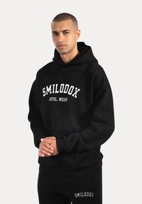 Czarna bluza z kapturem wykonana z miękkiego materiału, z przednią kieszenią i białym napisem "SMILODOX ATHL. WEAR" na klatce piersiowej. Standardowy krój.