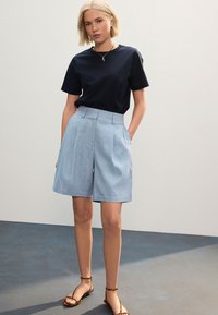 Maglietta blu navy a maniche corte abbinata a pantaloncini azzurri su misura con pieghe e sandali marroni con cinturini e motivo sottile.