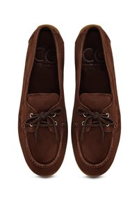 Brune ruskind loafers med rund tå, snørebånd foran og metaløjer. Har en beige gummisål og syninger langs overdelen.