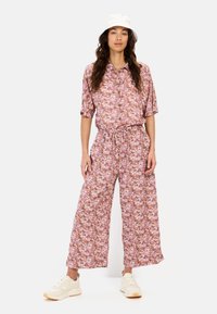 Bloemenprint bijpassende top en wijde broek in roze, oranje en wit, gemaakt van lichtgewicht stof. Model draagt een witte bucket hat en sneakers.