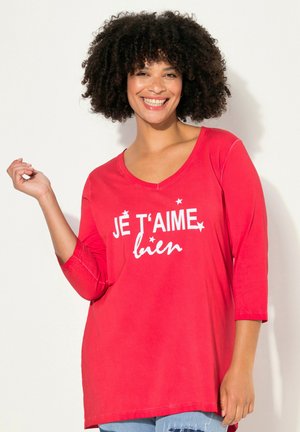 Maglietta rossa a maniche lunghe con scollo a V e testo bianco "JE T'AIME bien", caratterizzata da una vestibilità comoda e materiale soffice. Dettagli di cucitura visibili.