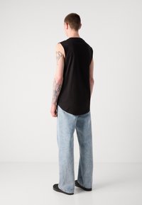 Top negru fără mâneci, cu o croială lejeră, asortat cu blugi evazați de culoare bleu deschis și pantofi negri. Tatuaj vizibil pe braț.