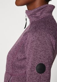 Fleecepullover, lila mélange-textur, hög krage med dragkedja, svart logotypapplikation på ärmen, figurnära design och kontrasterande sömnadsdetaljer.