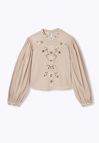 Blouse beige avec des motifs floraux brodés en crème et vert. Dotée de manches longues bouffantes et d'une ouverture en forme de clé au dos.