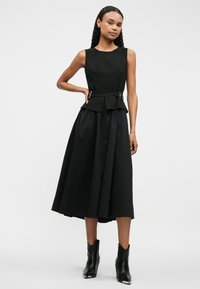 Μαύρο φόρεμα με εφαρμοστό κορμό, ζώνη peplum και φούστα που φουσκώνει. Διαθέτει ασημί μεταλλικά στοιχεία. Λεπτή υφή, μήκους γόνατος.