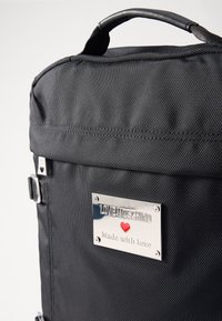 Black nylon backpack featuring a silver plaque with "LOVE MOSCHINO" and a red heart, and a textured surface with a top handle.